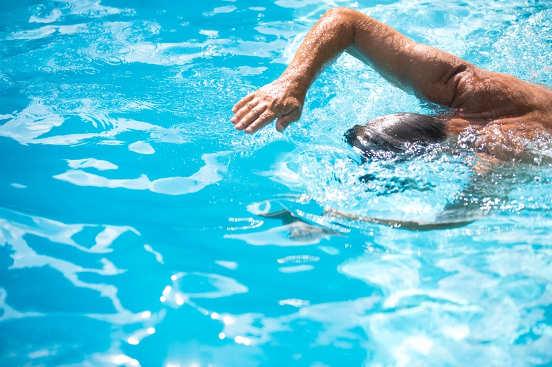 Man swimming laps in a pool, representing perseverance and post-surgery recovery.